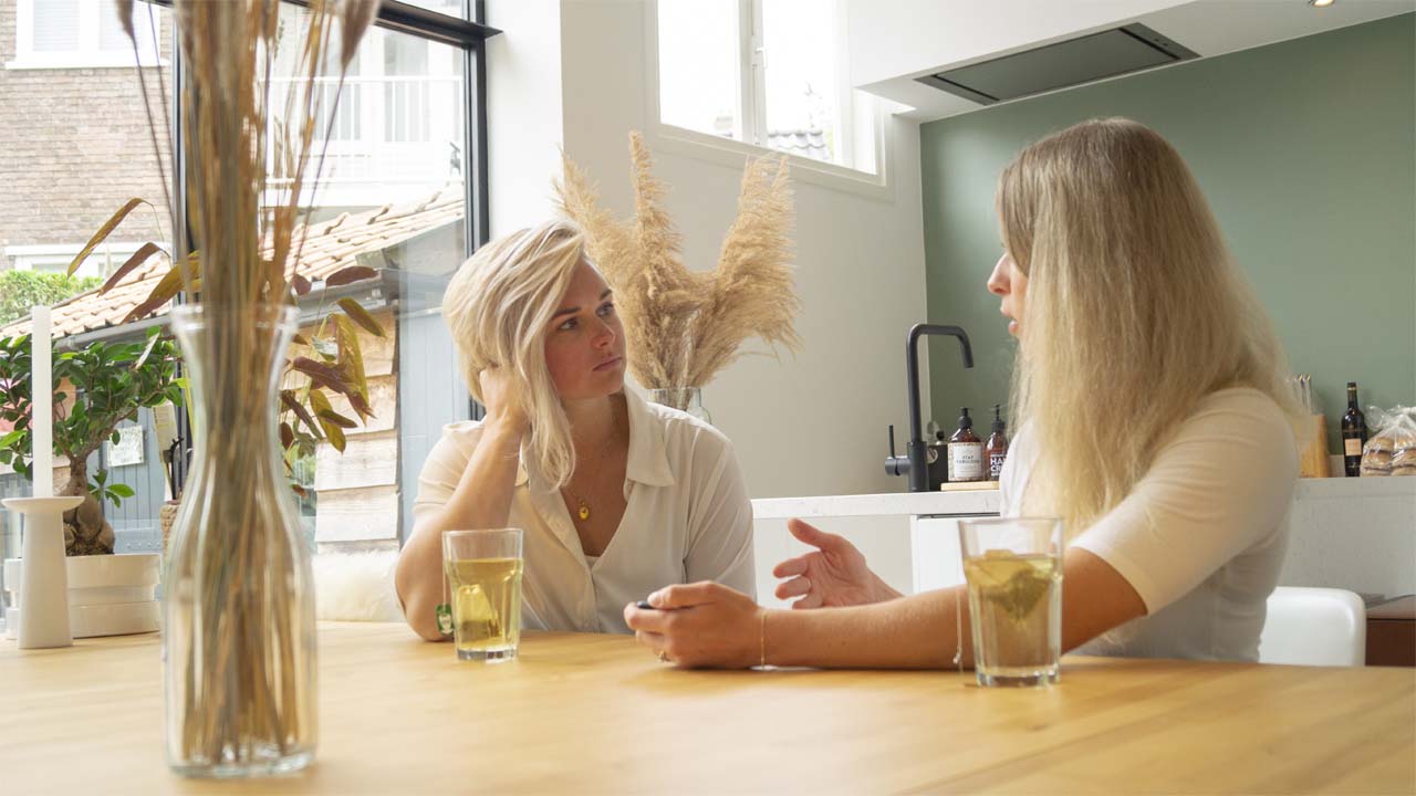 Leefstijl coach die een gesprek voert met een vrouwelijke client zittend aan een tafel in een woonkamer