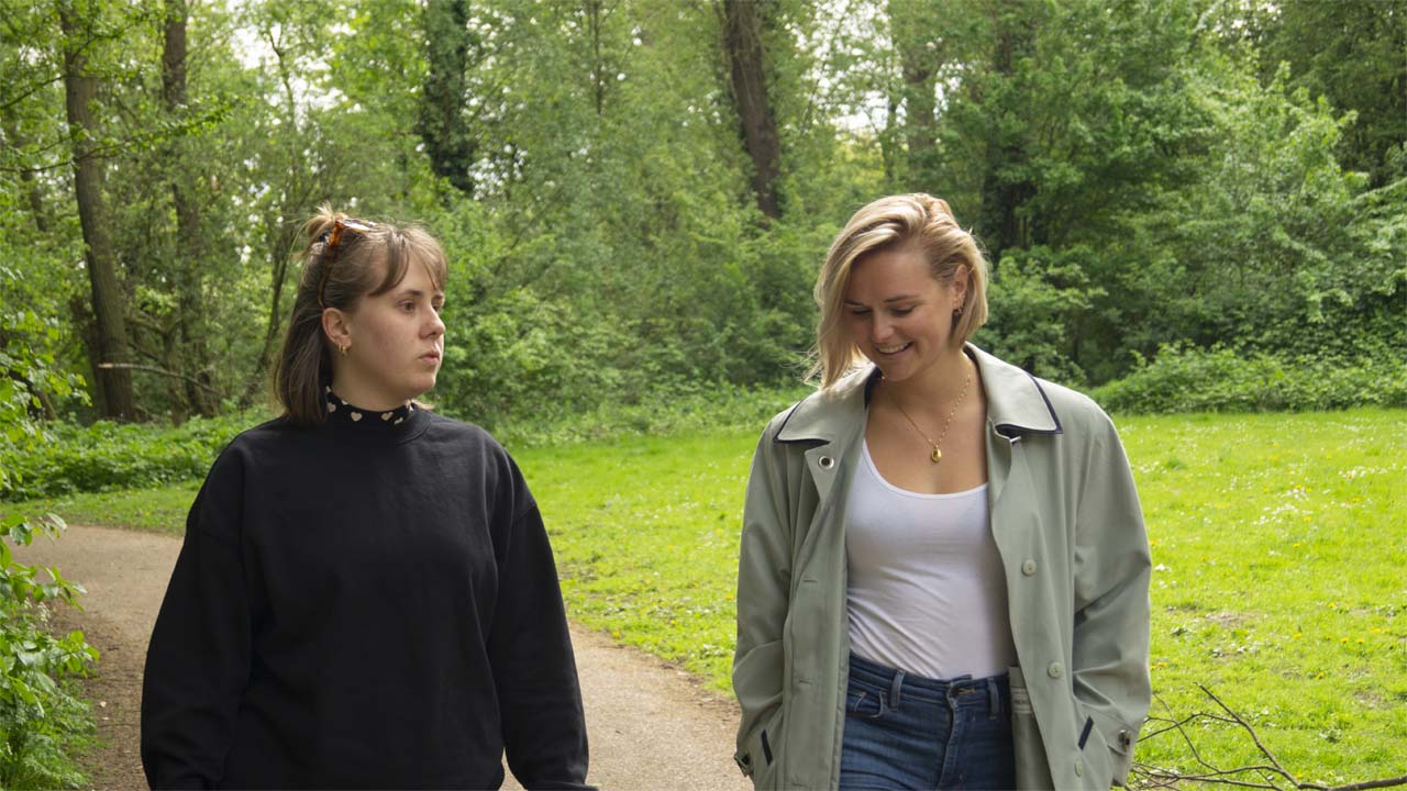 Leefstijl coach die een gesprek voert met een vrouwelijke client lopend in een park met bomen op de achtergrond.